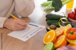 Woman writing a meal plan at a table adorned with fresh oranges, reflecting a commitment to sustainable nutrition.