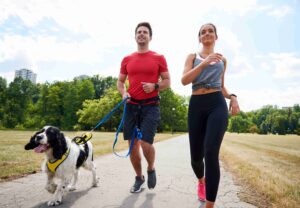 A couple joyfully running with their dog along a scenic trail, exemplifying the benefits of partner and pet workouts in fostering a sustainable fitness routine.