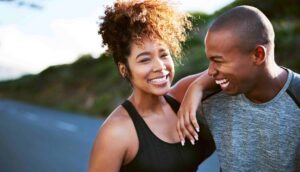 A joyful young couple jogging together outdoors in athletic attire, exemplifying a shared commitment to a sustainable fitness routine.