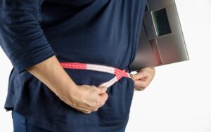 Guy measuring his waist with a tape measure. It is a simple way to check if you’re carrying excess body fat around your middle.