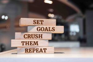 Wooden blocks stacked with the words 'Set goals, crush them, repeat' — illustrating the motivation and accountability a personal trainer provides.