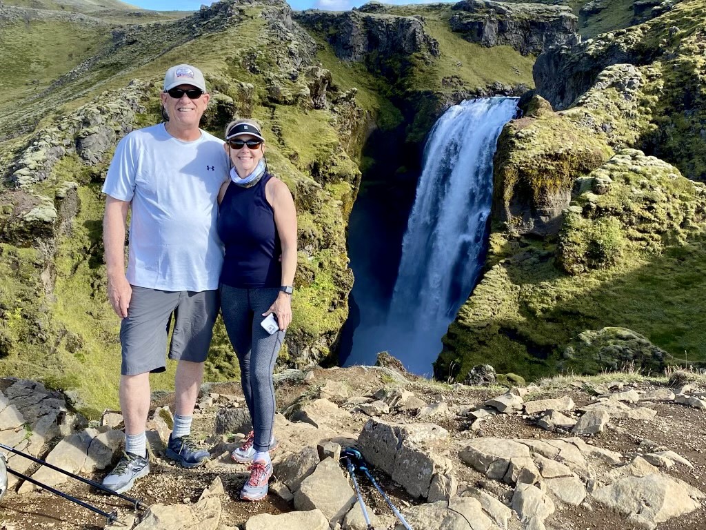 A couple clad in sportswear pause for a photo up against the backdrop of a gentle waterfall.