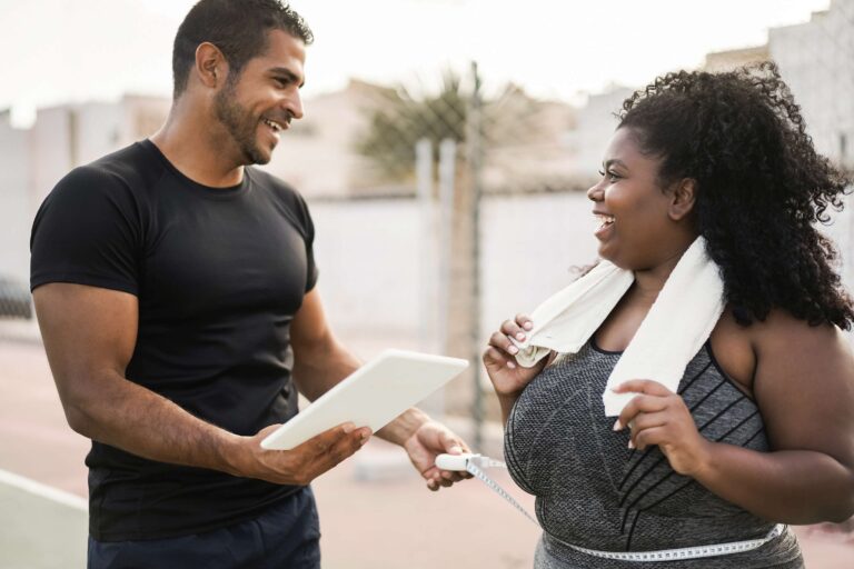 Woman discussing her weight loss training program with her personal coach, as the trainer measures her waist.