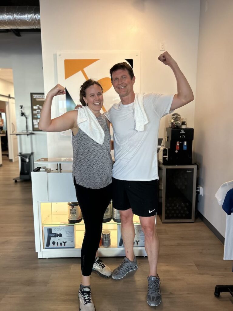 Two clients flex after a workout at Pledge To Fitness, a personal training studio in Bellaire, with towels around their necks.