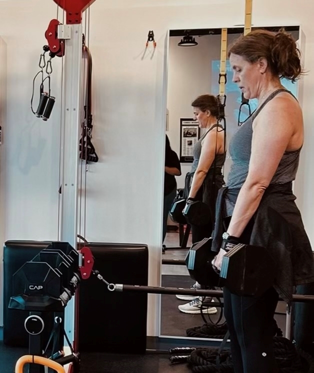 Woman holding dumbbells at her sides in Pledge To Fitness® studio in Bellaire TX.