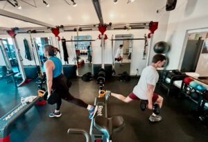 Man and woman performing Bulgarian split squats with dumbbells at Pledge To Fitness® studio, Bellaire, TX
